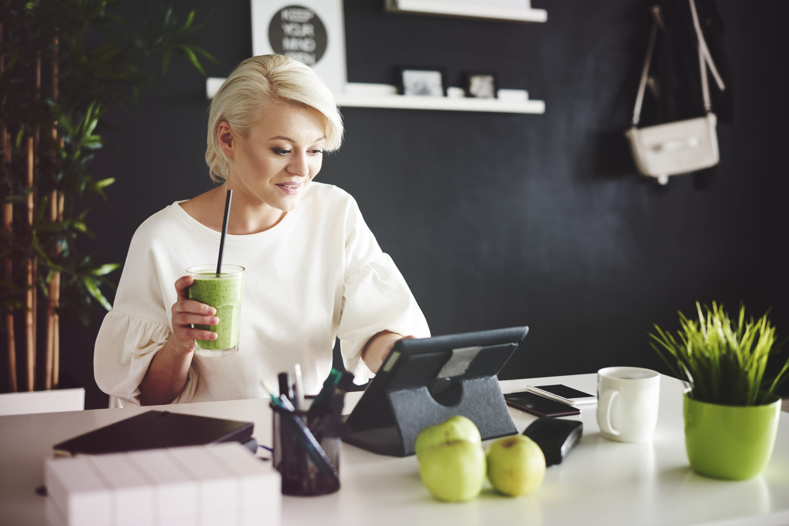 Woman with smoothie using a digital tablet at her desk on her business blog